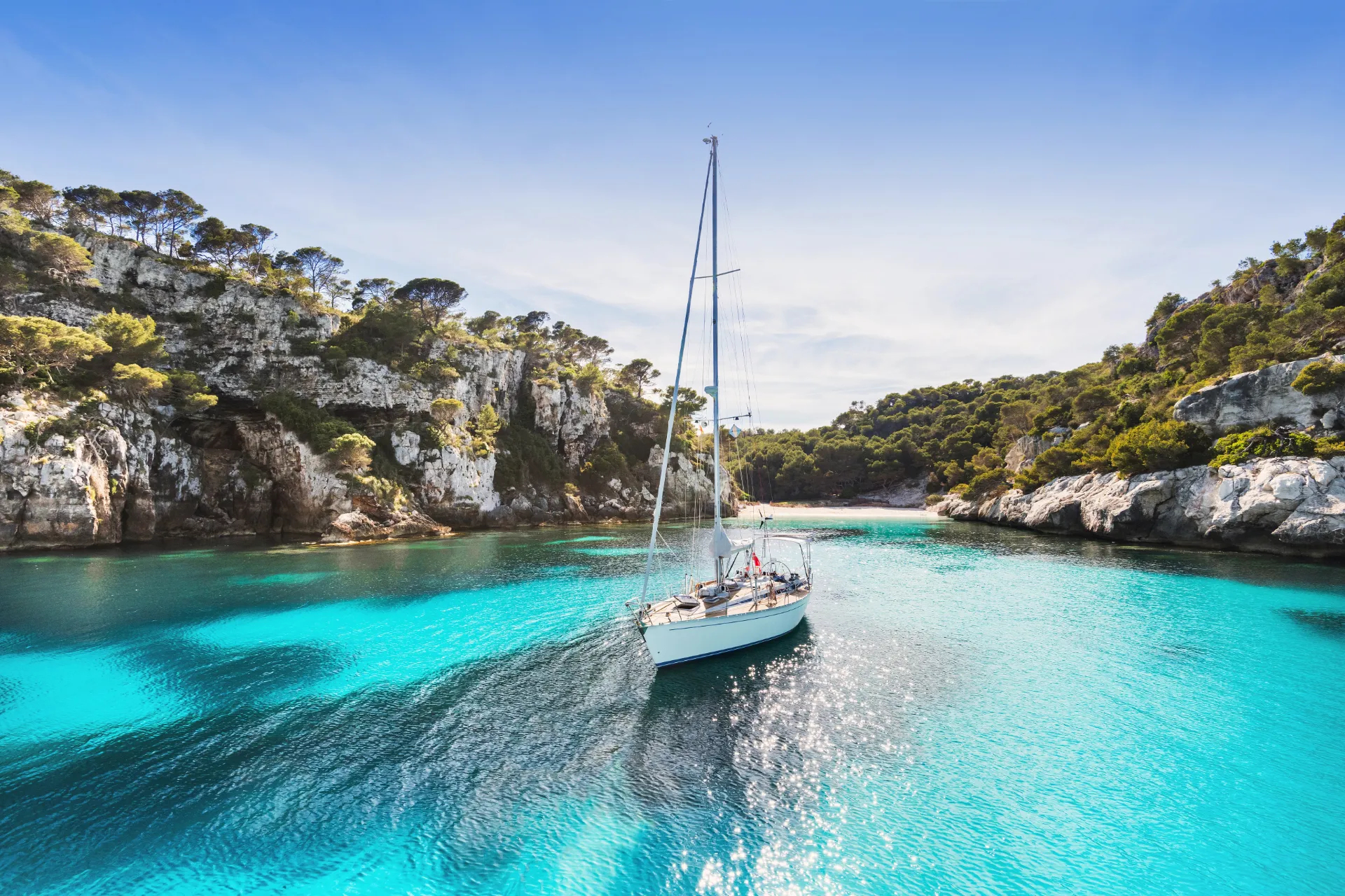 Strand auf Menorca mit Segelboot im Meer.