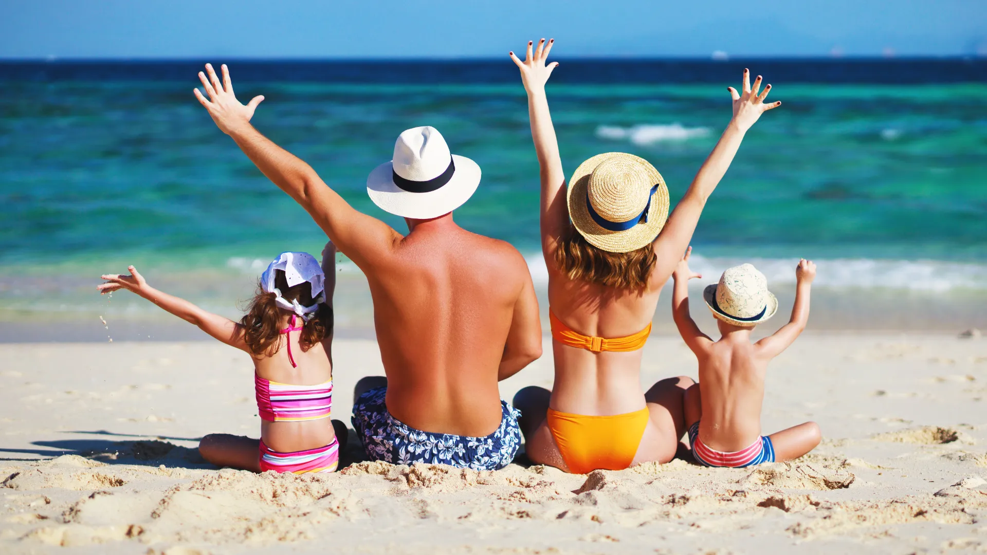 Familie von hinten am Strand mit Blick auf das Meer.